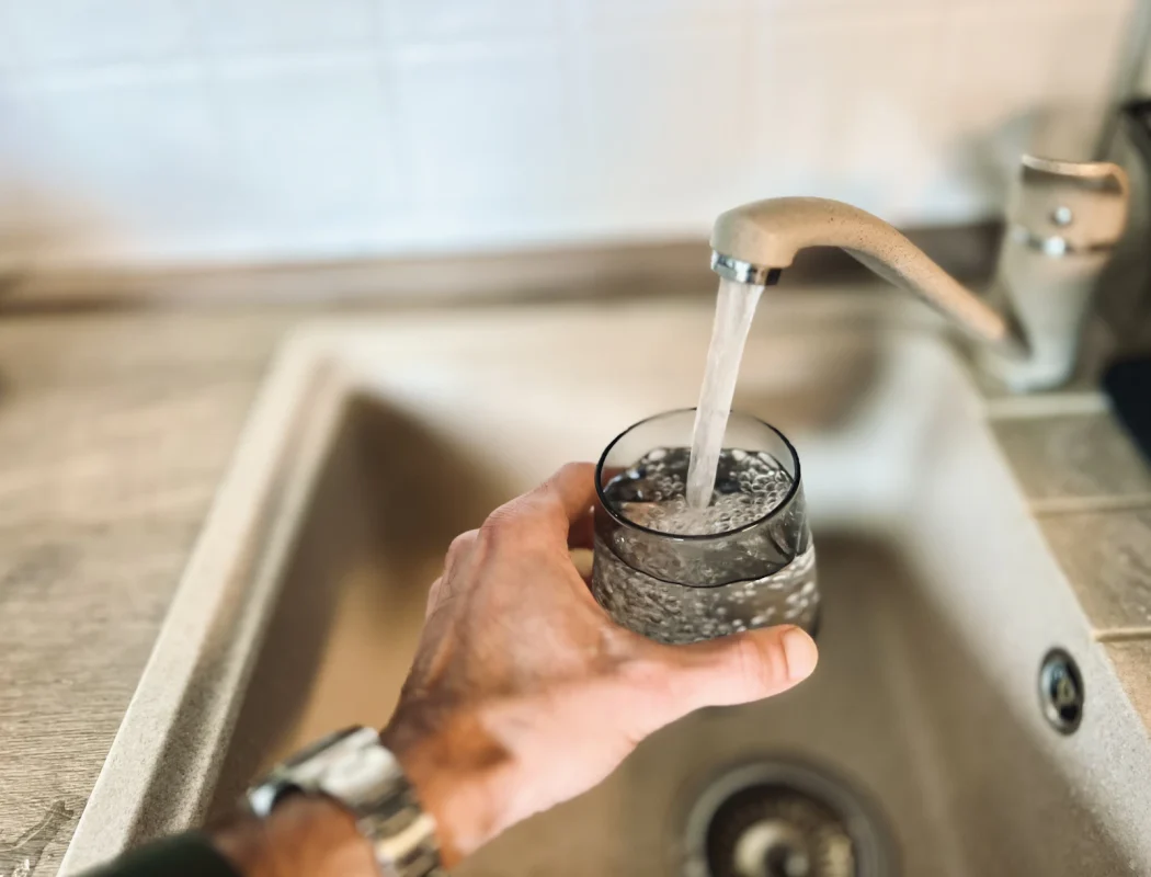 Mano che riempie un bicchiere con l'acqua del rubinetto della cucina